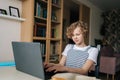 Portrait of little Caucasian school girl using typing on laptop sitting at table with paper textbook, studying online at Royalty Free Stock Photo