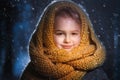 Portrait of a little charming girl in a yellow wool scarf standing outside during a snow blizzard Royalty Free Stock Photo