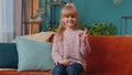 Portrait of little child girl kid alone on sofa at home showing ok gesture, like sign, positive good Royalty Free Stock Photo