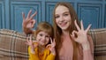 Portrait of little child kid daughter with young mother, hugging, embracing, showing ok gesture sign Royalty Free Stock Photo