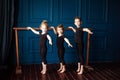 Portrait of 3 little children two girls ballerina and small boy dancer in black leotard practicing at ballet barre at dance studio