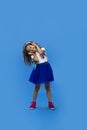 Little curly girl playing with big headphones, listening to music and dancing with closed eyes over blue background Royalty Free Stock Photo