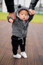 Portrait of little cute baby boy making first steps, holding hands of father and mother, looking at the camera Royalty Free Stock Photo