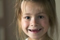 Portrait of little cute blond young child girl with gray eyes smiling in camera with funny toothless smile on blurred gray backgro Royalty Free Stock Photo