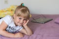 A portrait of little cute blonde caucasian girl sitting on a bed and dreamily smiling. Girl has big beautiful grey-blue colored ey Royalty Free Stock Photo