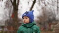 Portrait of little cute boy in a green jacket and hat with horns in the park