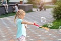 Portrait of little cute caucasian blond girl having fun and joy blowing big soap bubbles playing on city street park outdoors. Royalty Free Stock Photo