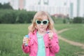 Portrait of little cute caucasian blond girl having fun and joy blowing big soap bubbles playing on city street park outdoors Royalty Free Stock Photo