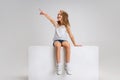 Portrait of little cute girl in casual clothes sitting on big box isolated on white studio background. Happy childhood Royalty Free Stock Photo