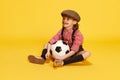 Portrait of little cute girl, child in shirt and shorts posing with football ball against yellow studio background Royalty Free Stock Photo