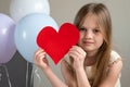 Portrait of little cute girl holding big red heart near air balloons. Valentines Day, love, mothers fathers Day