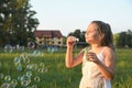 Portrait of little cute girl which blows soap bubbles smiling. Outdoors on a background of green grass and forest Royalty Free Stock Photo