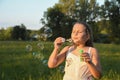 Portrait of little cute girl which blows soap bubbles smiling. Outdoors on a background of green grass and forest Royalty Free Stock Photo