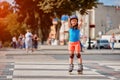 Portrait of little cute happy girl rollerblading through the city streets in the warm sunshiny summer day.