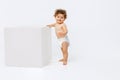Portrait of little cute toddler boy, baby in diaper cheerfully standing near cube and smiling isolated over white studio Royalty Free Stock Photo