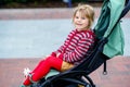Portrait of little cute toddler girl sitting in stroller or pram and going for a walk. Happy cute baby child having fun Royalty Free Stock Photo