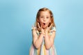 Portrait of little emotive girl, child standing with shocked face, looking at camera against blue studio background Royalty Free Stock Photo