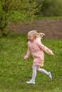 Portrait of little European girl with blonde hair in pink outfit running across field. Vertical frame Royalty Free Stock Photo