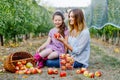 Portrait of little girl and beautiful mother with red apples in organic orchard. Happy woman and kid daughter picking Royalty Free Stock Photo