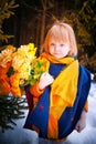 Portrait of Little girl in blue coat, yellow scarf and bouquet of flowers in winter or spring in nature in the Royalty Free Stock Photo