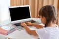 Portrait of little girl with braids having online lesson during distance education, sitting on table and typing on keyboard, Royalty Free Stock Photo