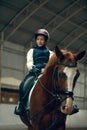 Portrait of little girl, child in helmet sitting on brown horse, training, practicing horseback riding. Royalty Free Stock Photo