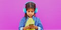 Portrait of little girl child with phone listening to music in wireless headphones over a pink Royalty Free Stock Photo