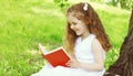 Portrait little girl child reading a book on the grass in summer park Royalty Free Stock Photo