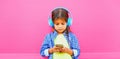 Portrait of little girl child with smartphone listening to music in wireless headphones on pink background in the city Royalty Free Stock Photo