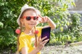 Portrait of little girl child taking a selfie by smartphone in summer park. A cheerful little girl shows a V gesture. Royalty Free Stock Photo