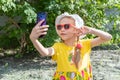 Portrait of little girl child taking a selfie by smartphone in summer park. A cheerful little girl in a yellow dress Royalty Free Stock Photo