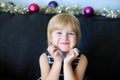 Portrait of little girl with Christmas decoration in the background. Child smiling, holding her head with hands, sitting on dark Royalty Free Stock Photo