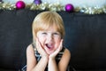 Portrait of little girl with christmas decoration in the background. Child smiling with surprise, holding her head with hands, Royalty Free Stock Photo