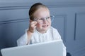 Portrait of little girl in eyeglasses behind laptop, over on a grey neo classic wall background