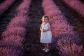 Portrait of little girl in flower dress stay among rows of purple lavender in field. Happy child Royalty Free Stock Photo