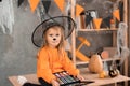 Portrait of a little girl in a Halloween costume sitting at the table with a palette of eyeshadows for makeup in a witch