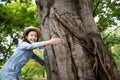 Portrait of little girl in hat with smiling,hugging large tree trunk and looking at camera in outdoor park,asian cute child with Royalty Free Stock Photo