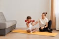 Portrait of little girl holding red dumbbells in hands, mother teaching her daughter to do sport exercises, sitting on floor on Royalty Free Stock Photo