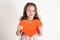 Portrait of little girl with long curly hair hold in hands big red paper heart smiling on white background. Copy space. Royalty Free Stock Photo