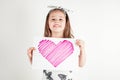 Portrait of little girl with long hair holding in hands sheet of paper with pink heart for present on white background.