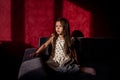 Portrait of little girl with long hair sits on sofa against red background of bright light shadow Royalty Free Stock Photo