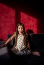 Portrait of little girl with long hair sits on sofa against red background of bright light shadow Royalty Free Stock Photo