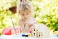 Portrait of little girl paints wooden model of house