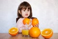 Portrait of a little girl plays with an oranges on a table. Happy little girl with glass of juice Royalty Free Stock Photo