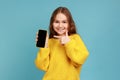 Portrait of little girl pointing finger at blank screen of mobile phone, looking smiling to camera. Royalty Free Stock Photo