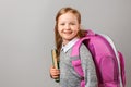 Portrait of little girl schoolgirl with backpack and book on gray background. Charming child student closeup. Back to school. The Royalty Free Stock Photo