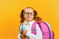 Portrait of little girl schoolgirl with backpack and book on yellow background. Charming child student closeup. Back to school. Royalty Free Stock Photo