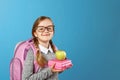 Portrait of a little girl schoolgirl in glasses with a backpack and lunch boxing on a blue background. Back to school Royalty Free Stock Photo