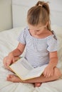 Little girl sitting on bed reading book