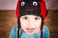 Portrait of little girl smiling and being happy. Child is wearing a woolen cap in the shape of ladybird on a background with red Royalty Free Stock Photo